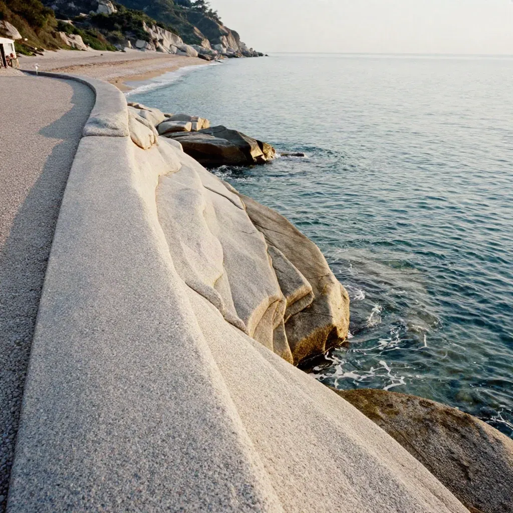 Rocce granitiche chiare, acqua bassa trasparente e parcheggio sopra la spiaggia.